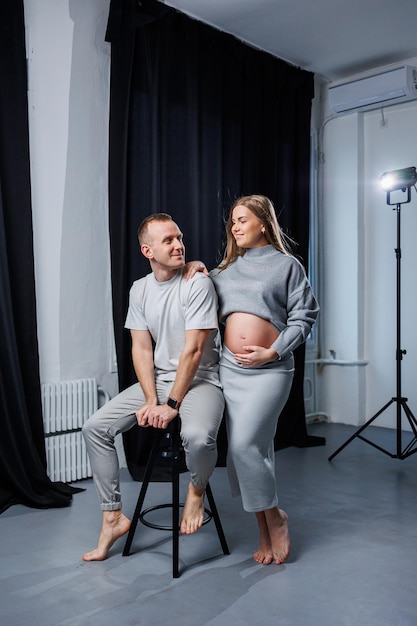 A smiling pregnant woman and her husband are standing in the studio and hugging Beautiful young attractive pregnant woman Family marriage childbirth concept Happy pregnant couple