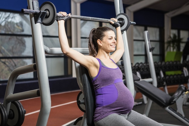 Smiling pregnant woman lifting barbell at the gym