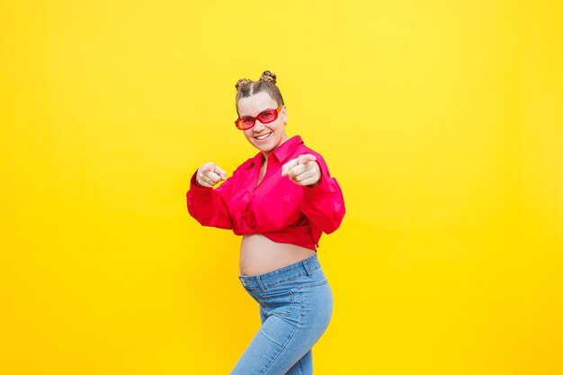 A smiling pregnant woman in a pink cotton shirt and jeans gently holds her pregnant belly Posing for the camera Concept of easy and happy pregnancy