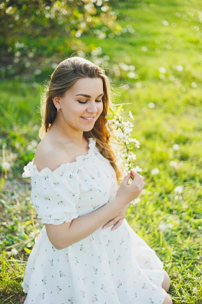 A smiling pregnant woman in a white light dress walks in a green spring garden A woman is expecting a child Happy pregnant woman in nature