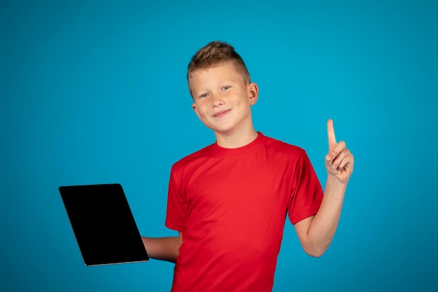 Smiling Preteen Boy Holding Blank Digital Tablet And Pointing Finger Up