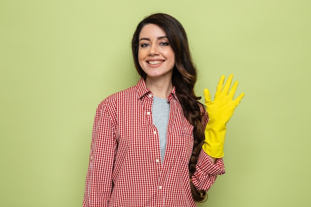 Smiling pretty caucasian cleaner woman with rubber gloves keeping hand open and looking at front