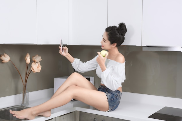 Smiling pretty woman taking a selfie with an apple in the kitchen.