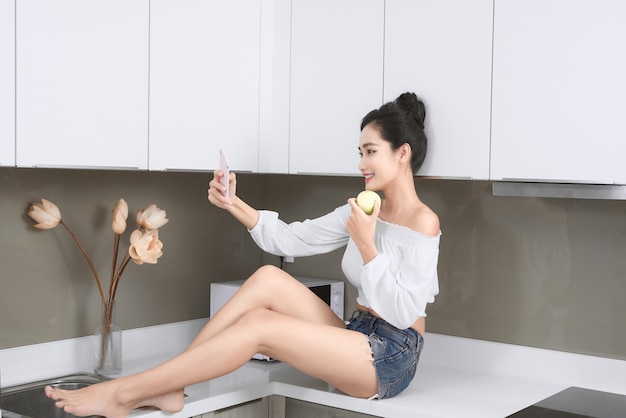 Smiling pretty woman taking a selfie with an apple in the kitchen.