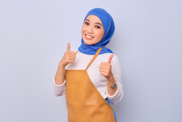 Smiling pretty young barista girl in apron showing thumb up gesture isolated on white background