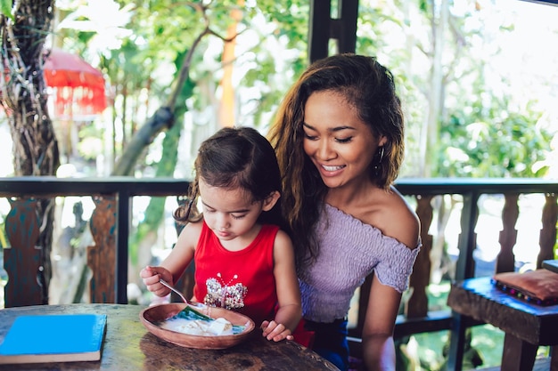 Smiling pretty young mother and cute little girl tasting food at restaurant