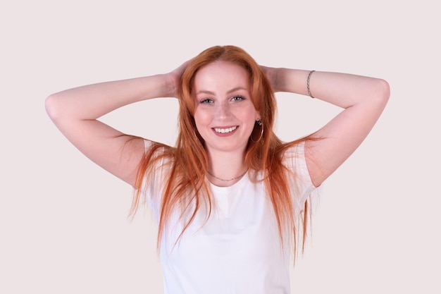 Smiling redhead young woman with tousled hair stretches on a light background