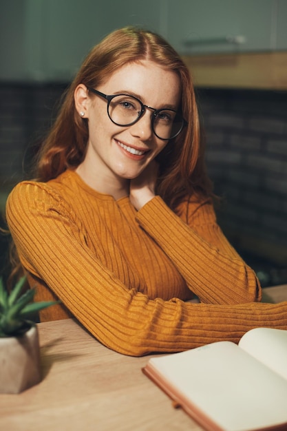 Smiling redheaded woman with eyeglasses reading a book dreaming and looking at camera beautiful youn