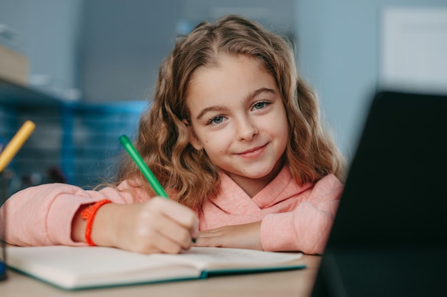 Smiling schoolgirl using tablet for studying talking at webcam online education coronavirus school d