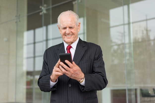 smiling senior business man browsing on smartphone at modern office building