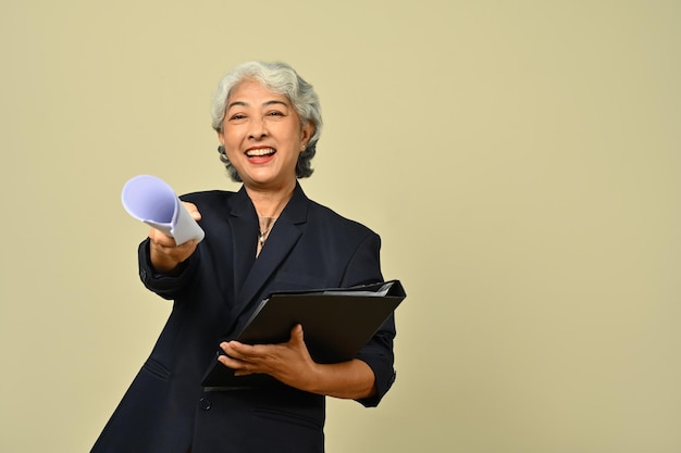 Smiling senior businesswoman wearing black suit and eyeglasses posing isolated on beige background