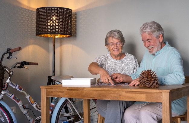 Smiling senior couple doing a jigsaw puzzle at home on wooden table Vintage bicycle in the corner