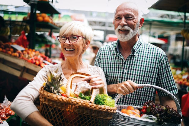 Smiling senior couple holding basket with vegetables at the grocery shop