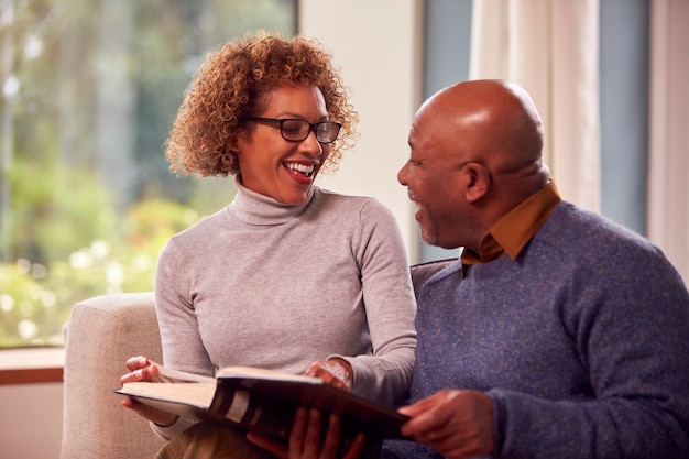 Smiling Senior Couple Sitting On Sofa At Home Looking Through Photo Album