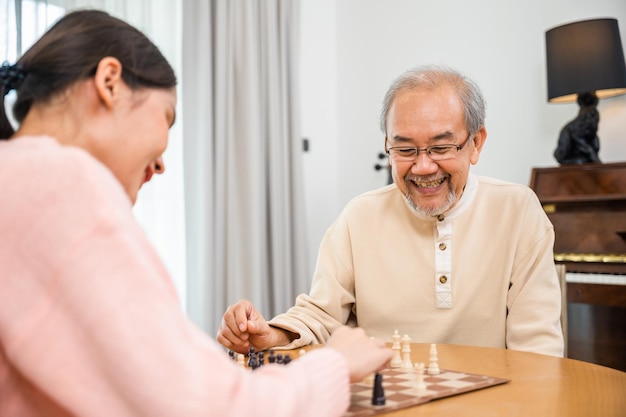 Smiling senior elderly having fun playing chess game with beautiful daughter at home, nurse caregiver in nursing home for leisure, Happy active retired people, Healthcare and medical homecare concept