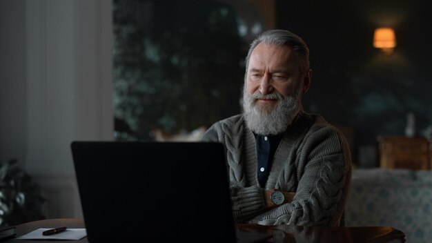 Smiling senior man calling video online at laptop computer at luxury house Old business man talking video conference at remote workplace Relaxed elderly man making video call at home office