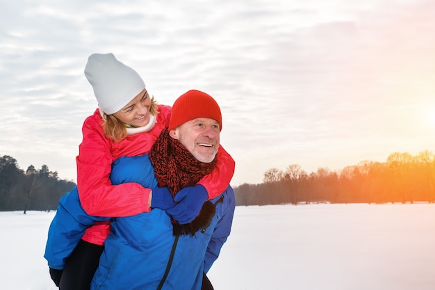 Smiling senior man giving mature woman piggyback in snowy winter park