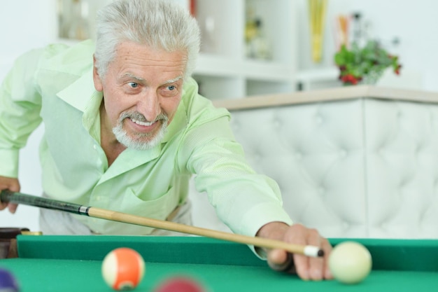 Smiling senior man playing billiard at home