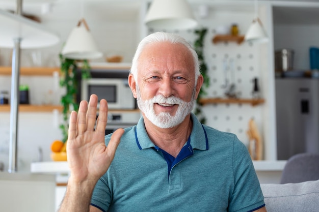 Smiling senior man wave to camera having video call on laptop happy elderly male sit on couch at home talk using modern technologies and wireless connection