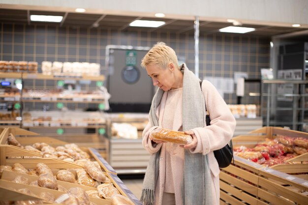 Smiling senior mature woman choosing bread and baking in grocery section of supermarket at the bakery store