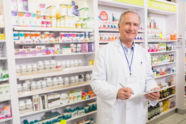 Smiling senior pharmacist writing on clipboard