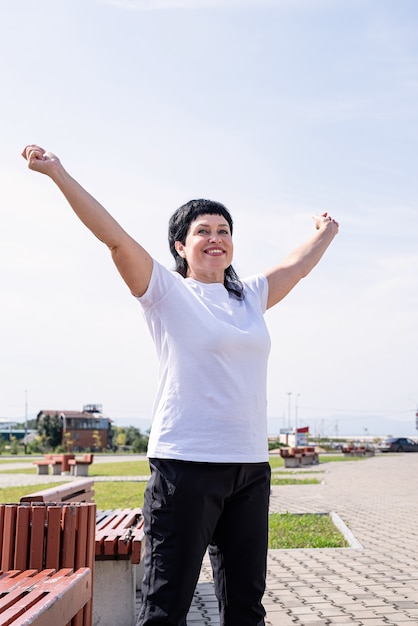 Smiling senior woman doing warm up before training outdoors in the park