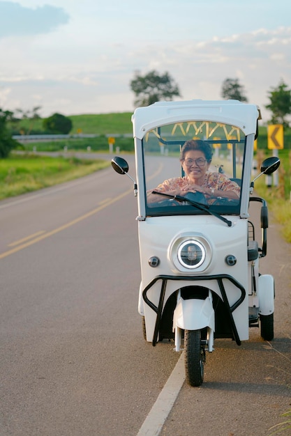 Smiling senior woman driving a electric tricycle on the road with rice field scenery