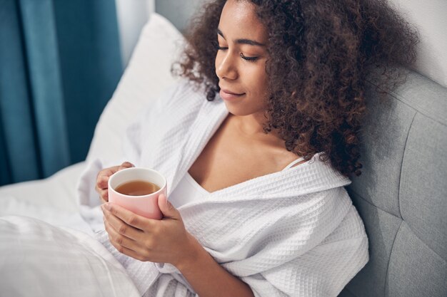 Smiling serene beautiful young lady sitting with her eyes closed in bed