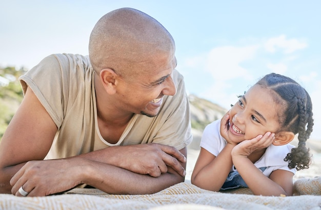 Smiling single father and little daughter looking at each other while relaxing on a beach Adorable girl bonding with her dad and enjoying vacation Man and child having fun and enjoying family time