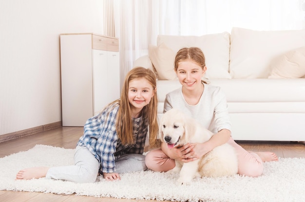 Smiling sisters sit together with retriever puppy