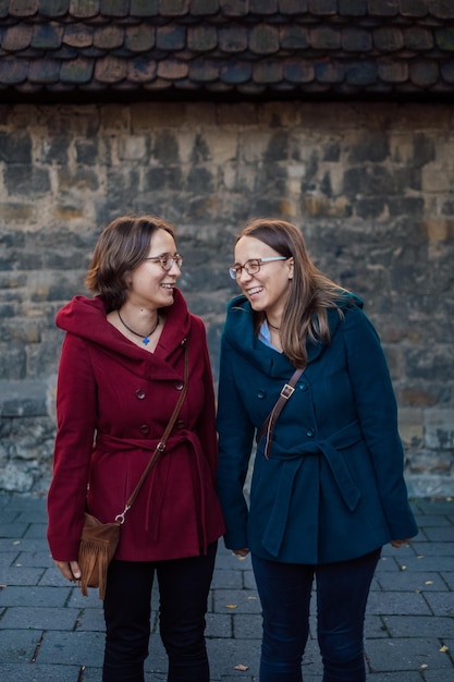 Photo smiling sisters standing against stone wall