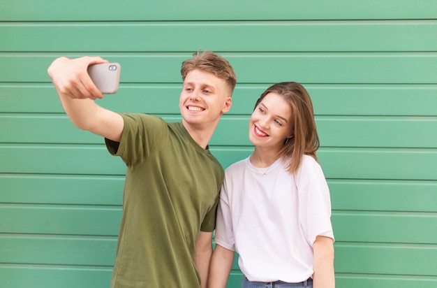 Smiling smiling couple makes a selfie on the of a green wall wearing a stylish summer casual clothing.