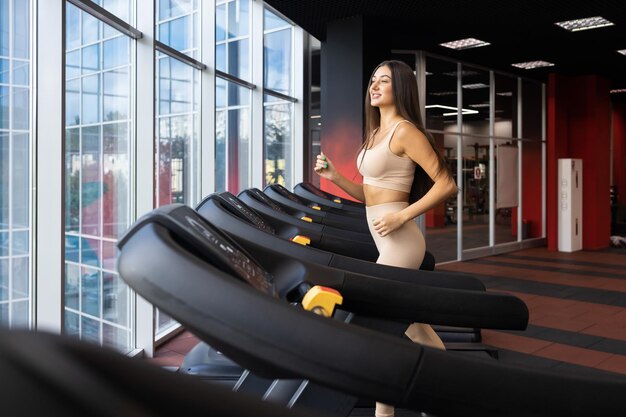 Smiling sportive girl running on a treadmill while exercising in the gym