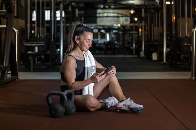 Smiling sportswoman using smartphone while resting after training in gym