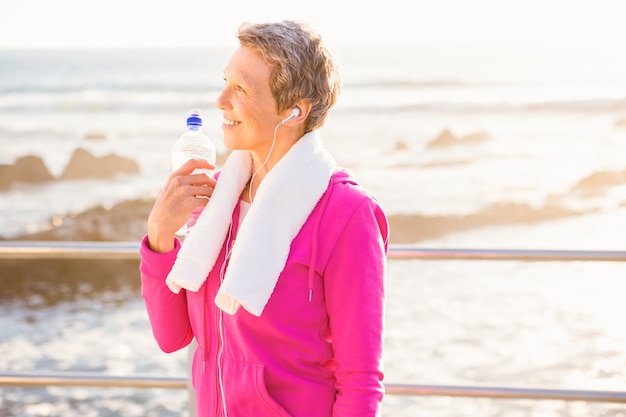 Smiling sporty woman with water bottle listening to music 