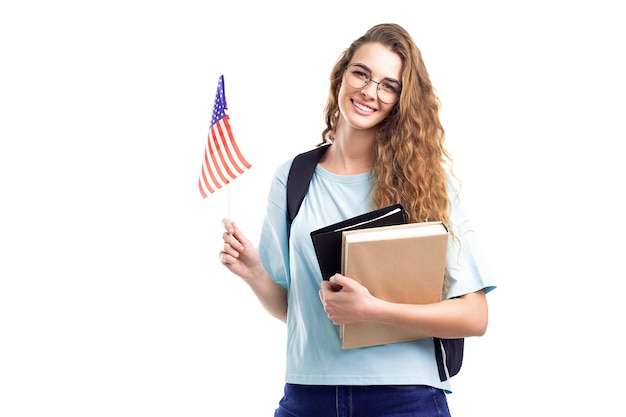 Smiling student girl in glasses with backpack holds books notebooks and flag usa on white background