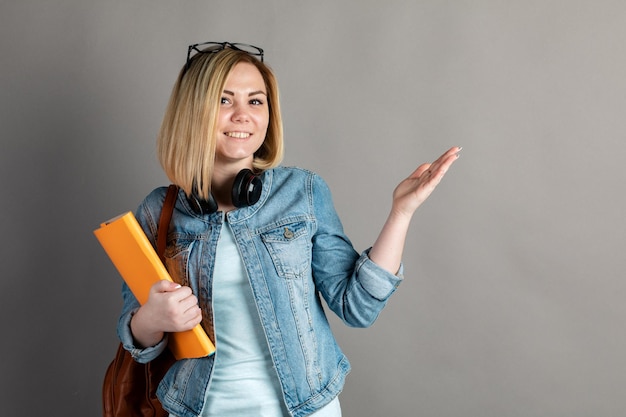 Smiling student with backpack and book isolated on grey background