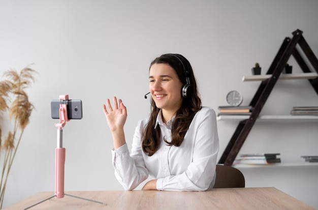 Smiling student with a wireless headset has an online lesson from home via a smartphone standing on a tripod View of the phone camera of a young teacher in headphones online communication for text