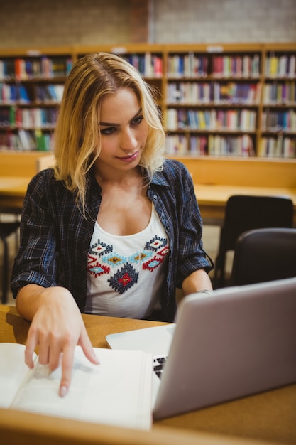 Smiling student working while using her laptop in library