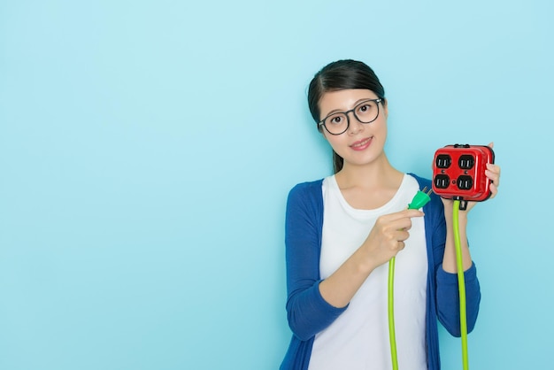 smiling sweet woman wearing lifestyle clothing holding electricity device face to camera and showing saving electric concept standing in blue background.