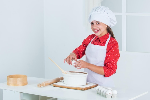 Smiling teen girl in chef uniform cooking and baking food