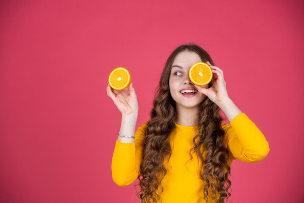 Smiling teen girl hold orange fruit on pink background