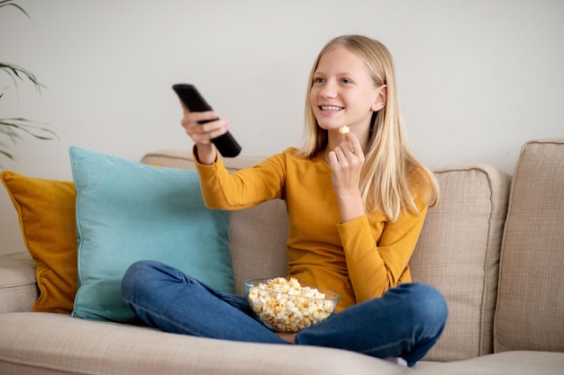 Smiling teen girl watching tv and eating popcorn on a couch