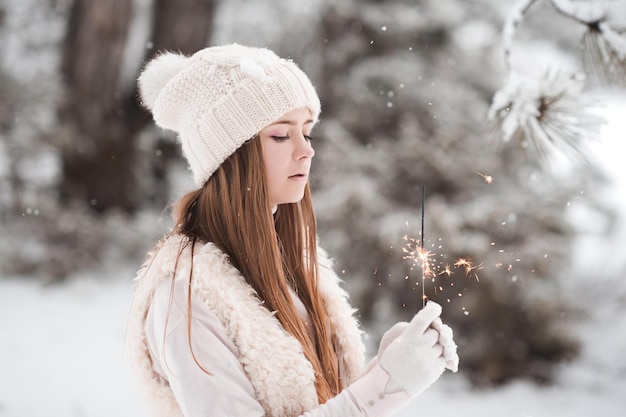 Smiling teen girl wearing winter knitted clothes holding sparkler outdoors