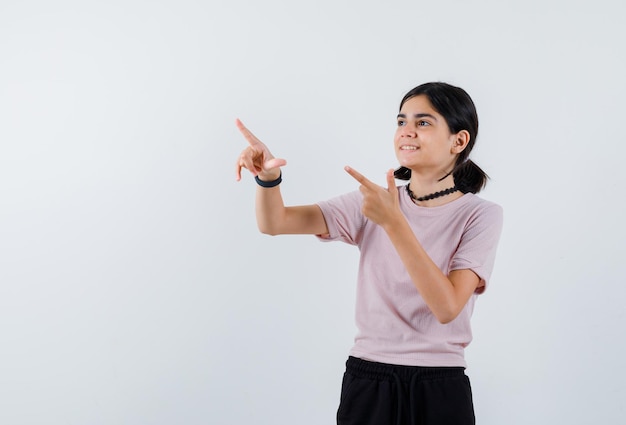 The smiling teenage girl is pointing to left with her forefingers  on white background