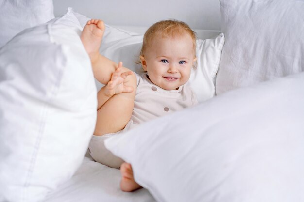 Smiling toddler with leg up having fun on bed with lots of pillows Baby exersising in stretching