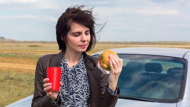 A smiling woman against a blue sky is about to eat a hamburger.