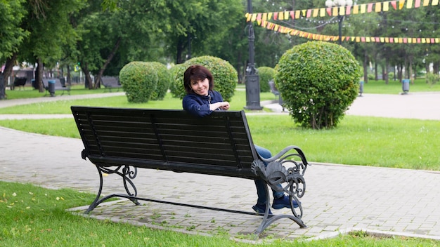 A smiling woman on a bench in a city park against the background of decorative bushes in the form of balloons