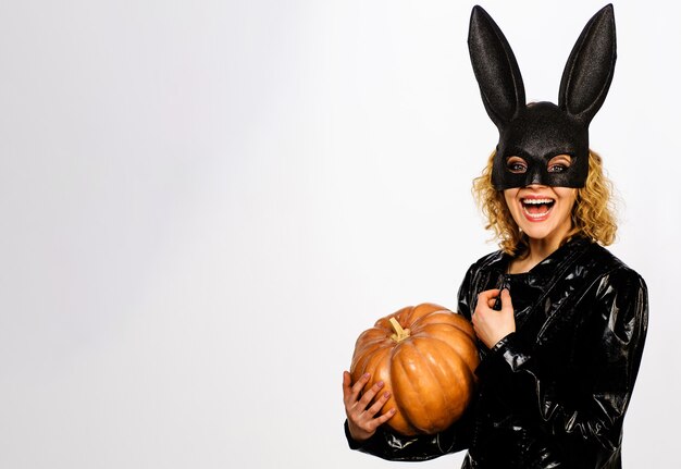 Smiling woman in black bunny mask with pumpkin. 31 October. Sexy girl in Halloween costume with jack-o-lantern.