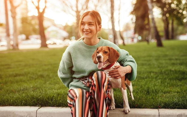 Smiling woman bonding adorable dog and siting on grass